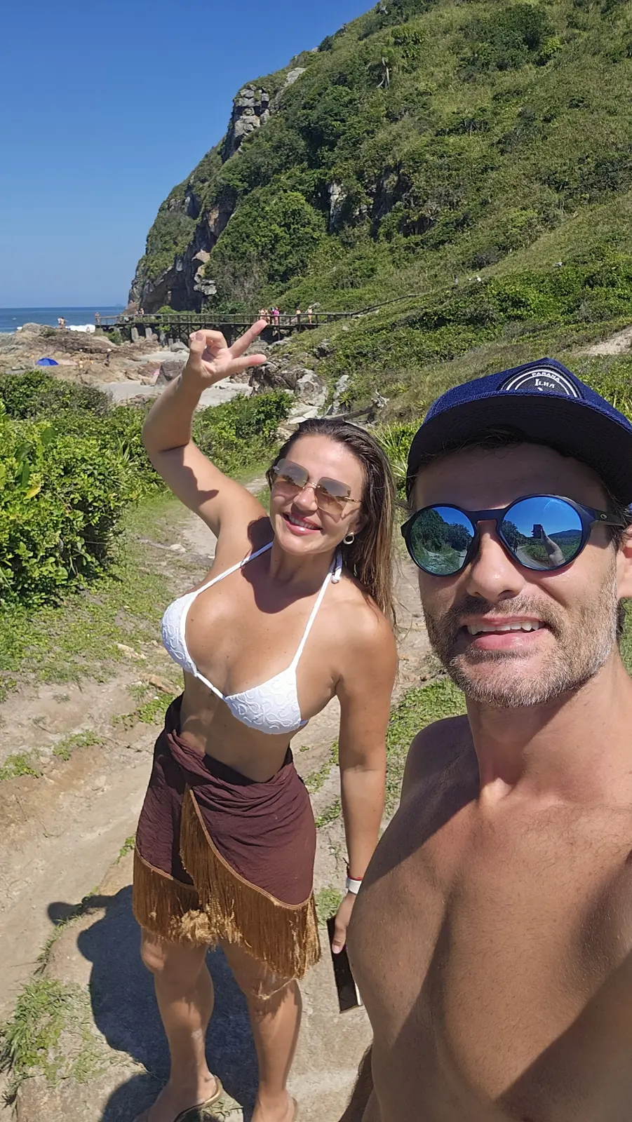 Ju e Vini na trilha da Ilha do Mel, com o morro e a passarela ao fundo